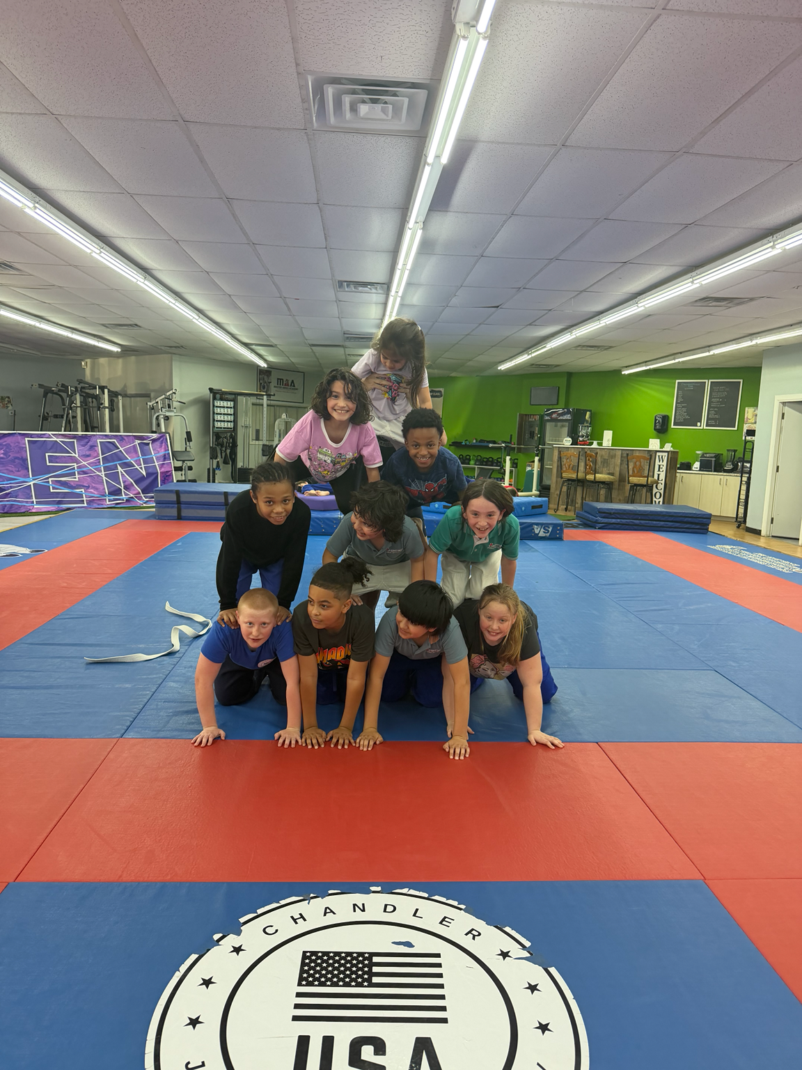 Children smiling while making a human pyramid on the mats inside Chandler Judo Academy.